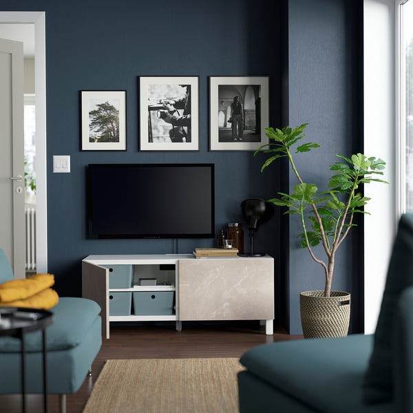 Modern living room with BESTÅ tv bench, adjustable shelves, and dark blue wall with teal sofa and plant.