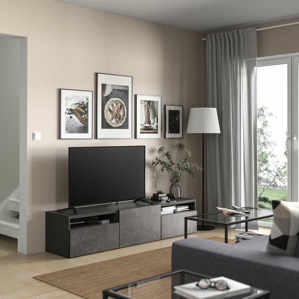Modern living room with BESTÅ tv unit, flat-screen tv, glass coffee table, gray curtains, and framed photos on beige walls.