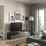 Modern living room with BESTÅ tv unit, flat-screen tv, glass coffee table, gray curtains, and framed photos on beige walls.