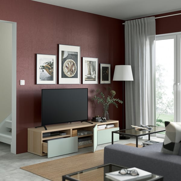 Modern living room with maroon walls, BESTÅ tv bench, white accents, grey sofa, and potted plant. A cozy, organized space.