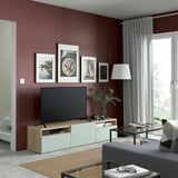 Modern living room with tv, dark red wall, framed pictures, lamp, grey curtains, coffee table items, grey sofa.