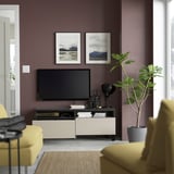 Modern living room with purple walls, tv on stand with drawers, yellow chairs, and plant.