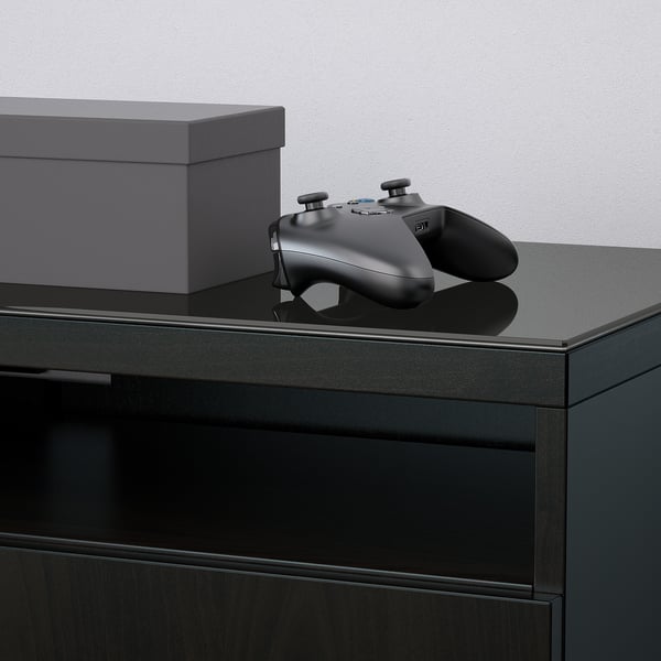 Black game controller rests on sleek, glass-topped tv stand, showcasing modern elegance and sturdy design.