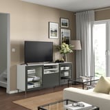 Modern living room with BESTÅ tv stand, flat screen tv, white flowers, and large window with curtains.