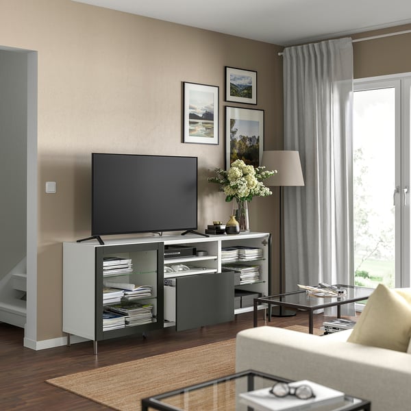 Modern living room with BESTÅ tv unit featuring a flat screen tv, decorative flowers, and framed artwork on beige walls.