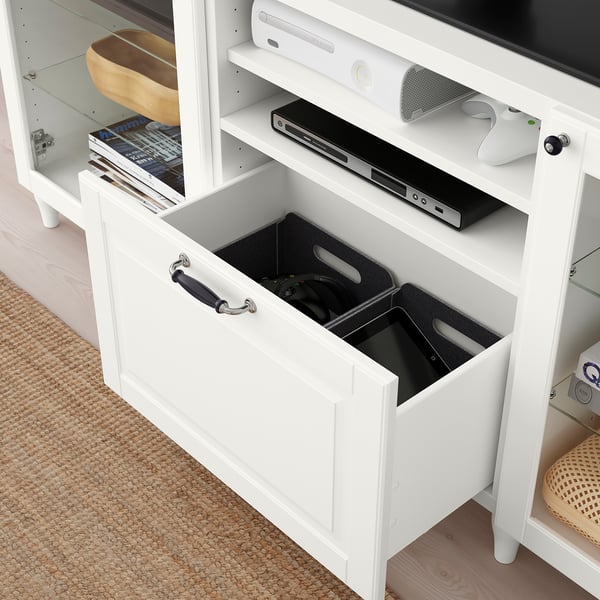 White BESTÅ tv bench with open drawer holding gaming controllers and a dvd player on top shelf.