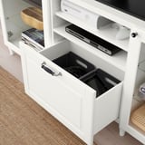 White BESTÅ tv bench with open drawer holding gaming controllers and a dvd player on top shelf.