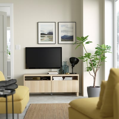 Modern living room with BESTÅ tv stand, flat screen, yellow chairs, plant, and art. Slim, uncluttered design.
