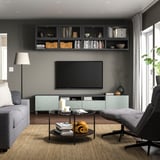 Modern living room with gray BESTÅ tv stand, shelves, and furniture. Flat screen tv, coffee table with books and blanket, gray sofa, and floor lamp.