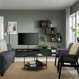 Modern green living room with gray sofa, tv on storage unit, large windows.