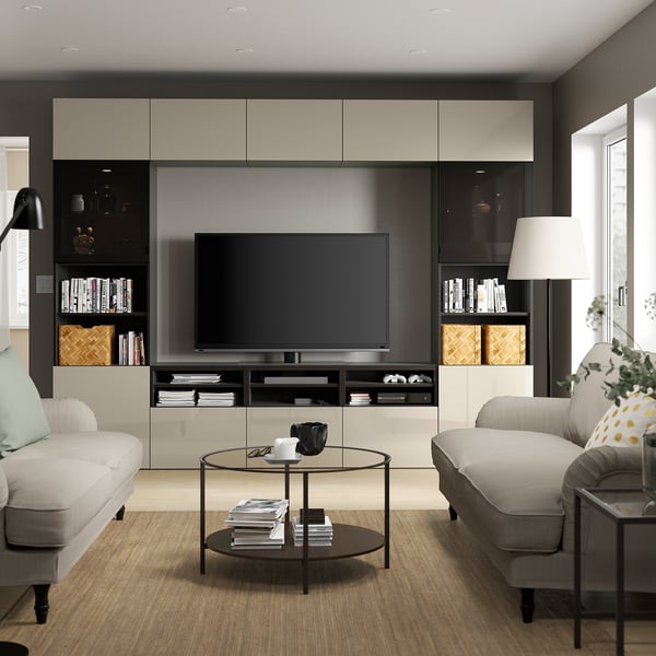 Modern living room with tv, grey couches, glass table, yellow pillow, lamp, wood floor, large windows.