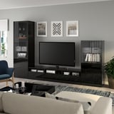 Modern living room with large tv on BESTÅ stand, sound system, books, and decor. Gray walls, sofa, coffee table, chair, and plant.