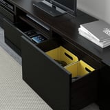 Black tv stand with open drawer showing yellow organizer and gaming controller, situated near gray sofa.