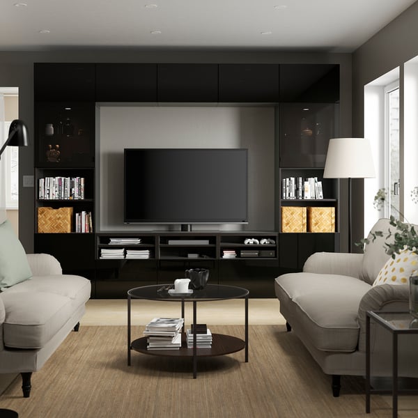Modern living room BESTÅ black entertainment center with tv, flanked by grey sofas. Centered coffee table holds books and remote controls.