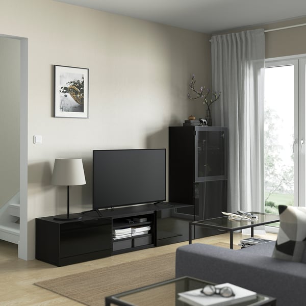 Modern living room with black BESTÅ tv stand, flat screen tv, glass coffee table, gray curtains, and white lamp.