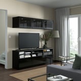 Modern living room with BESTÅ black tv stand, glass cabinet, tv, curtains, couch, wooden floor, and glass coffee table.