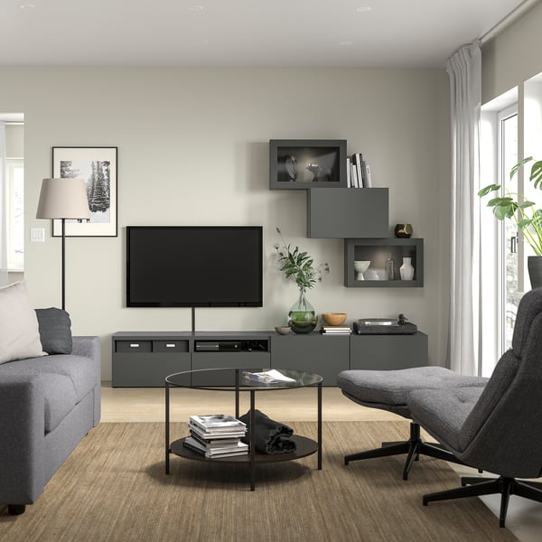 Modern living room with BESTÅ tv bench in gray, featuring a flat-screen tv, gray furniture, wooden floor, a glass coffee table, and minimalist decor.
