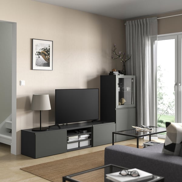 Modern living room with BESTÅ tv bench, flat-screen, storage, and glass shelves. Grey rug and curtain decor.