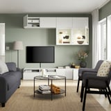 Modern living room with a grey sofa, glass coffee table, and a large tv on a white storage unit below wall-mounted cabinets.