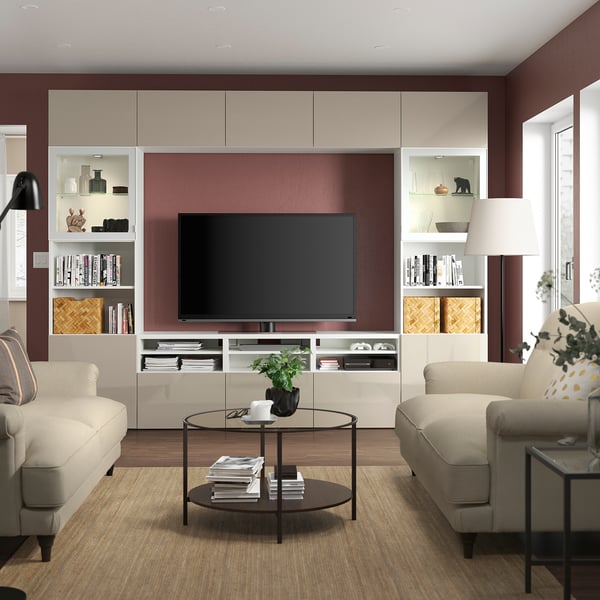 Modern living room with grey tv unit, two beige sofas, coffee table, and lamp against burgundy wall.