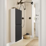 Modern black and white cabinet with sleek handles, integrated led lamp, and woven basket below, set against a light-colored wall.