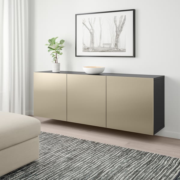 Modern living room with BESTÅ wall-mounted cabinet in light brown and black, between sofa and striped rug, with plant and bowl on top.