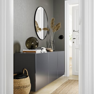 Modern entryway with dark grey BESTÅ unit, round mirror, dried plants, books, and wicker basket.