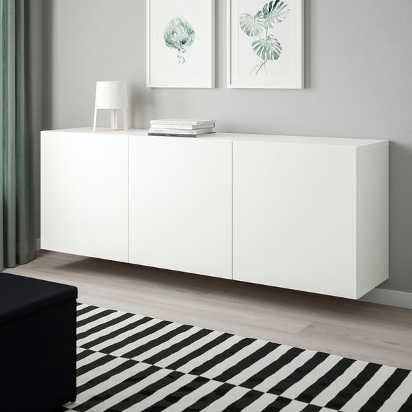 White BESTÅ wall-mounted cabinet; modern, minimalist design; larger than black ottoman, smaller than framed art.