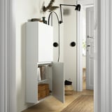 White wall-mounted cabinet, open doors showing books and boxes, black wall lamp above.