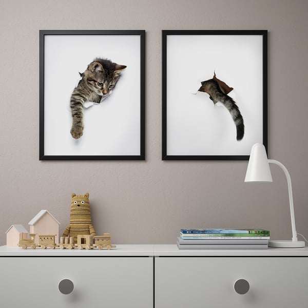 Two cat-themed picture frames hang above a cabinet with knickknacks and a lamp.