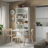 Modern minimalist dining area with white BILLY bookcase-desk combo, light wood chairs, and built-in cabinets.