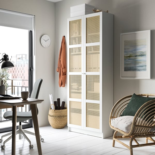 Modern home office with BILLY white and bamboo bookcase, gray desk, chair, clock, painting, and wicker chair with cushion.