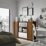 Cozy room with BILLY bookshelf, plants, chair, and geometric wallpaper.