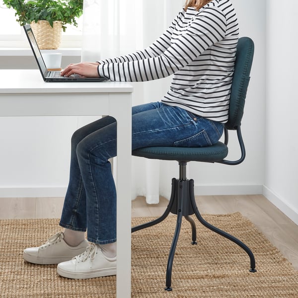 Person sitting in a black and green office chair at a white desk, typing on a laptop.