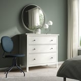Minimalist bedroom with blue BJÖRKBERGET chair, round mirror, lamp, and plant on dressing table. Gray bed partially visible.
