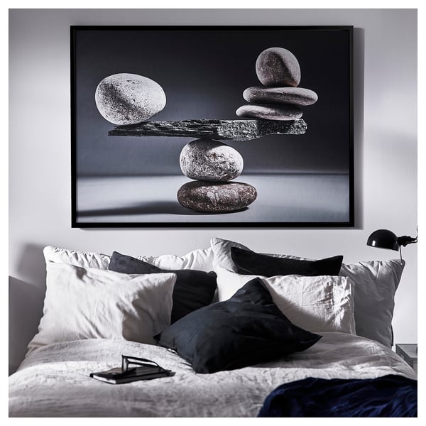 Bedroom with BJÖRKSTA black & white art, white bed with black & gray pillows, nightstand, lamp, phone.