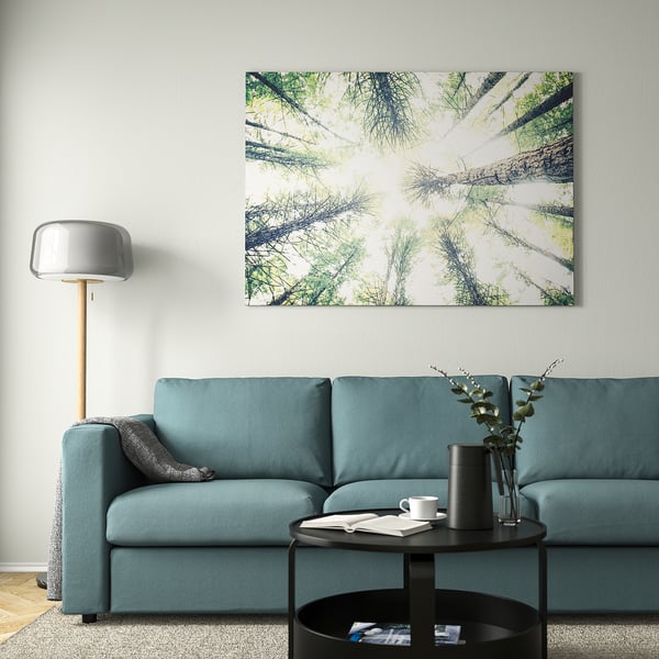 Modern living room with BJÖRKSTA forest picture, teal sofa, and minimalist lamp.