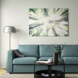 Modern living room with BJÖRKSTA forest picture, teal sofa, and minimalist lamp.