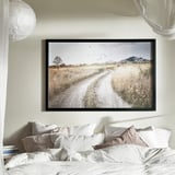 Large, black-framed landscape art above a cozy bed with white and beige pillows.