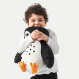 A young child hugs a soft penguin-shaped pillow, suitable for napping, made from recycled materials.