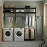 Modern laundry room with BOAXEL dark grey wall storage, ironing board, machines, and wicker baskets.