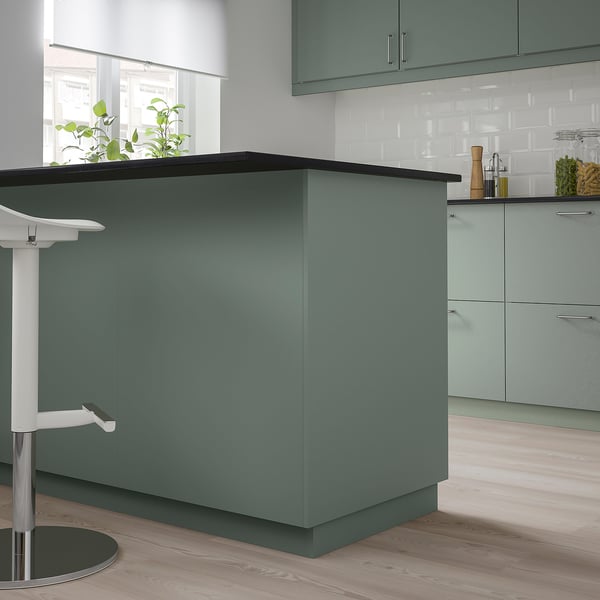 BODARP green kitchen island, modern design, medium size, with grey-green cabinets, wood floor, white stool, plant, and utensils.