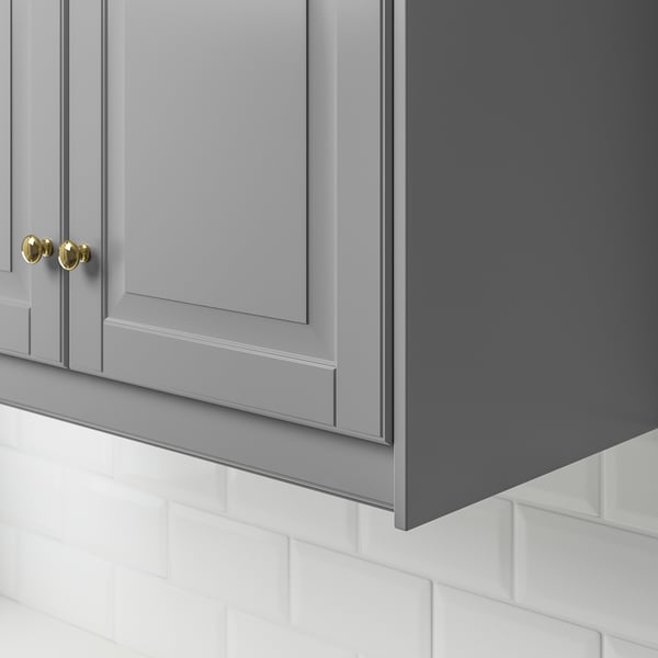 Grey kitchen cabinet with golden knobs, under which a white tile backsplash is visible.