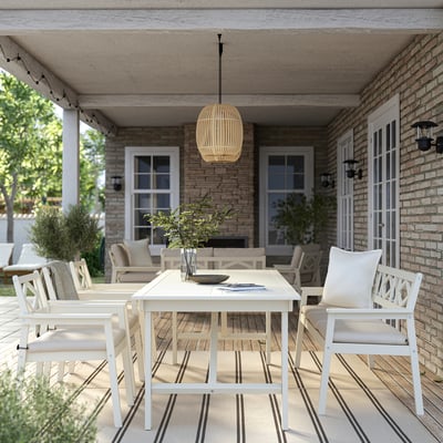 Under covered patio, large white acacia BONDHOLMEN outdoor table, cushioned chairs, hanging light.