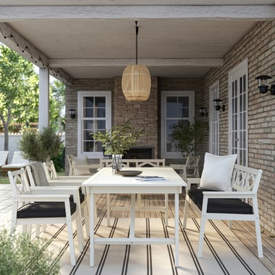 Modern outdoor dining set: white acacia table, cushioned chairs, hanging lamp, on a porch with brick walls and plants.