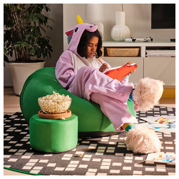 Person in unicorn onesie sits comfortably on green inflatable lounge, enjoying snacks and reading.