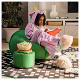 Person in unicorn onesie sits comfortably on green inflatable lounge, enjoying snacks and reading.