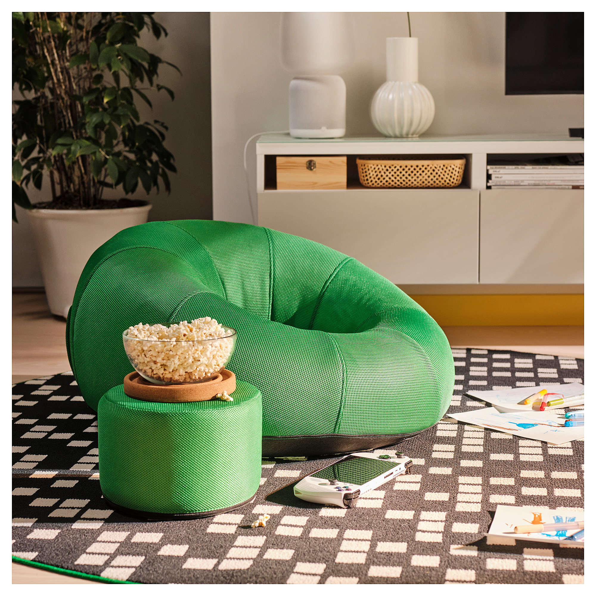 Bright green inflatable fauteuil chair BRÄNNBOLL on geometric rug. Bowl of popcorn on stool, plant, clean decor. Compact yet inviting.