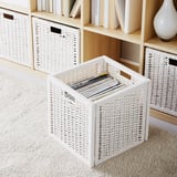 White woven rattan storage baskets on beige carpet, some filled with books, next to a wooden shelf.