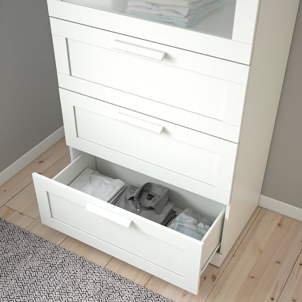 White chest of drawers with glass top, one open drawer revealing folded clothes. Anchored for safety.